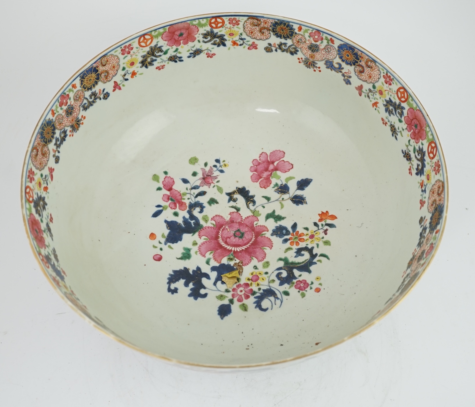 A large Chinese famille rose punch bowl, Qianlong period, the exterior painted with flowers in a fenced garden, the interior with a flower bouquet within a garland of flowers, 40.5cm diameter, wood stand. Condition - som